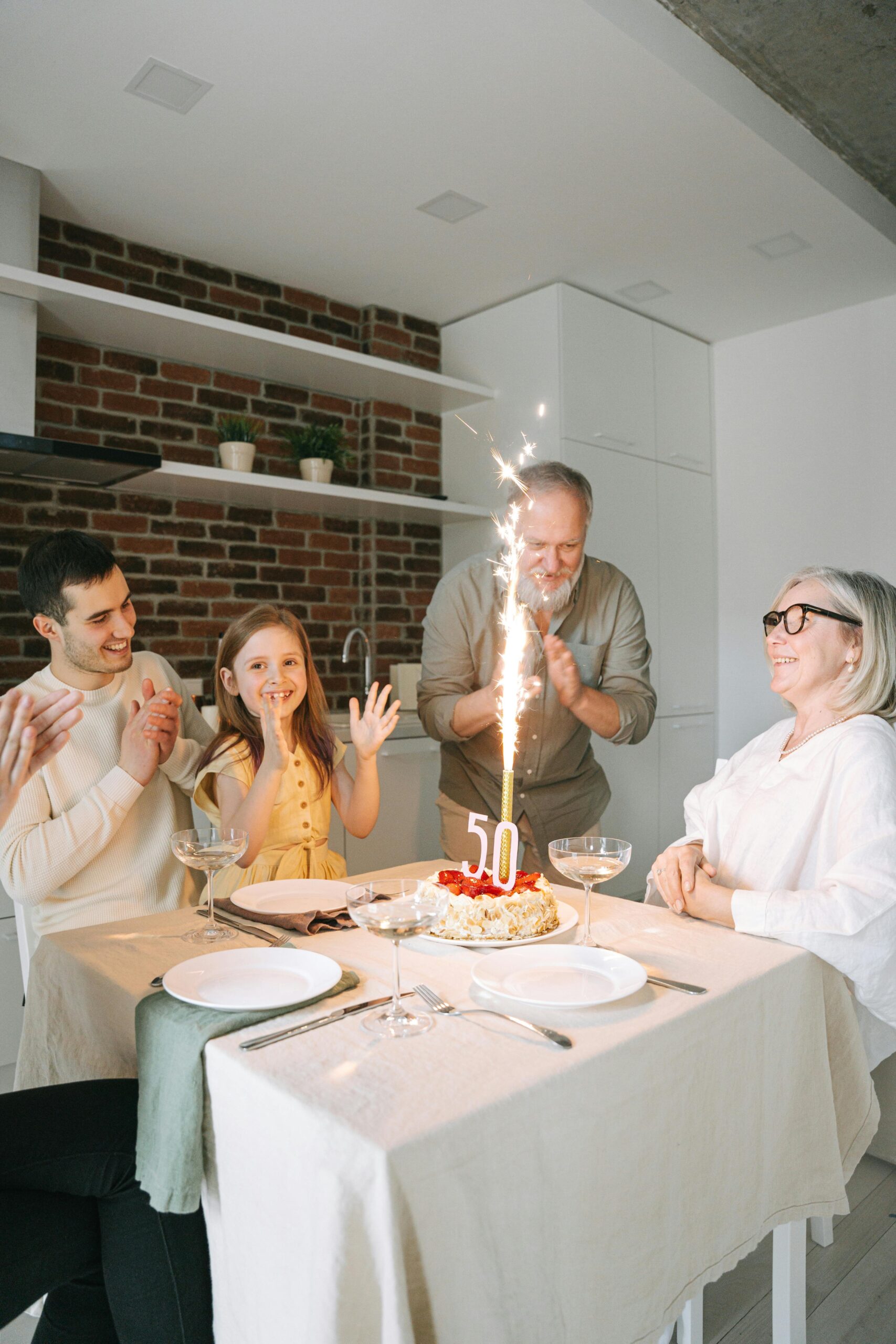 A joyful family celebration of a 50th birthday with a cake and sparklers in a modern kitchen.